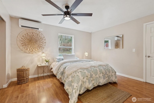 bedroom featuring a wall mounted air conditioner, ceiling fan, baseboards, and wood finished floors