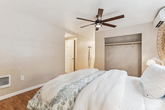 bedroom featuring baseboards, a ceiling fan, a wall unit AC, wood finished floors, and a closet