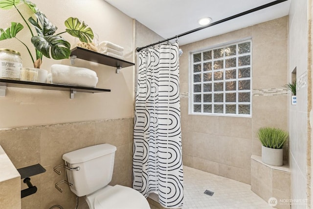 full bath featuring toilet, plenty of natural light, a tile shower, and tile walls