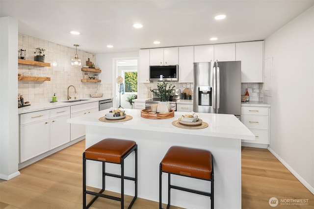 kitchen with a sink, a kitchen breakfast bar, light countertops, appliances with stainless steel finishes, and open shelves