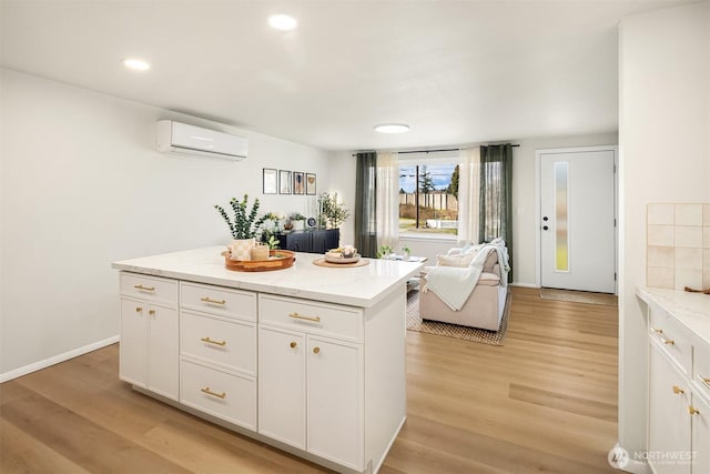 kitchen with light stone counters, a center island, white cabinetry, light wood-type flooring, and a wall mounted air conditioner