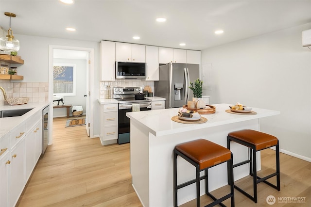 kitchen featuring a breakfast bar, a sink, light countertops, appliances with stainless steel finishes, and light wood finished floors