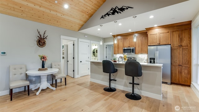 kitchen featuring stainless steel appliances, light wood-style flooring, brown cabinetry, an island with sink, and a kitchen bar