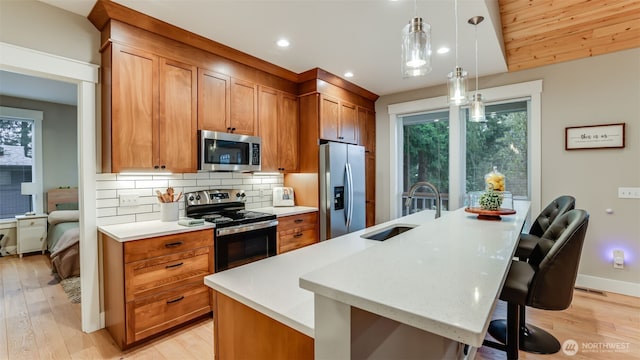 kitchen featuring a spacious island, light countertops, decorative backsplash, appliances with stainless steel finishes, and a sink