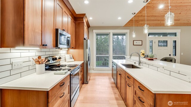 kitchen with appliances with stainless steel finishes, brown cabinetry, a sink, and a center island with sink