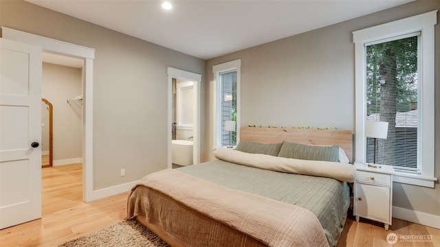 bedroom featuring light wood-type flooring, ensuite bath, baseboards, and a spacious closet