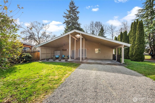 mid-century home with gravel driveway, a carport, and a front yard