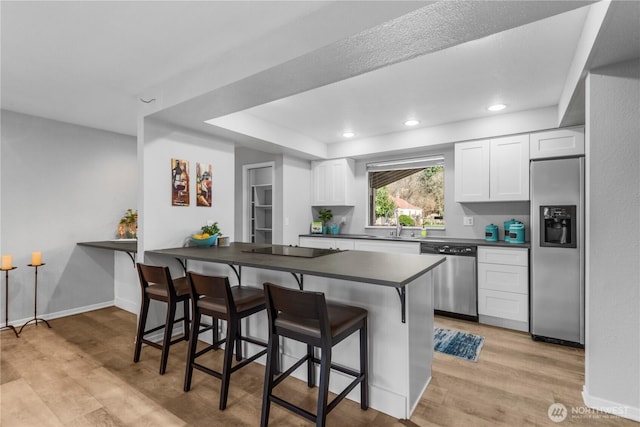 kitchen featuring appliances with stainless steel finishes, dark countertops, light wood-style flooring, and a kitchen breakfast bar