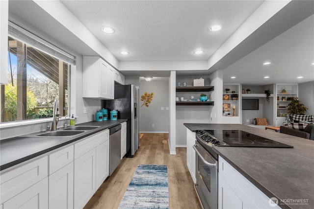 kitchen featuring dark countertops, light wood-style flooring, stainless steel appliances, open shelves, and a sink