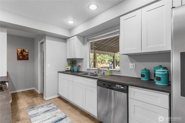 kitchen featuring light wood finished floors, dark countertops, appliances with stainless steel finishes, white cabinetry, and a sink