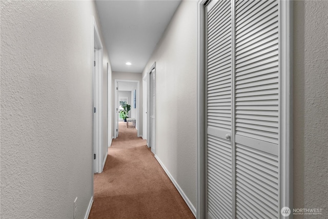 corridor with a textured wall, carpet floors, and baseboards