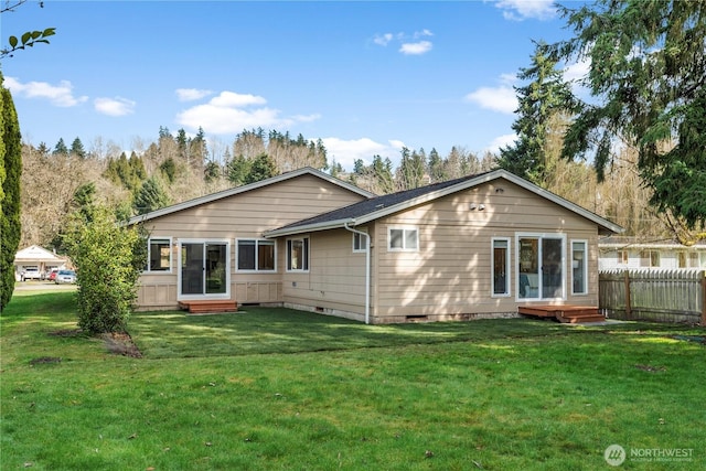 rear view of property featuring entry steps, fence, and a lawn