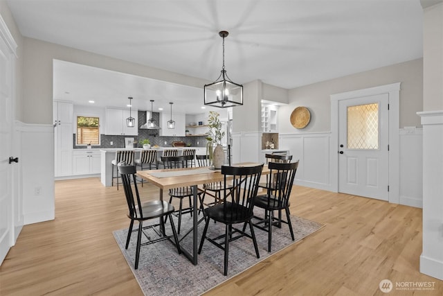 dining space featuring wainscoting, light wood-style flooring, and a notable chandelier