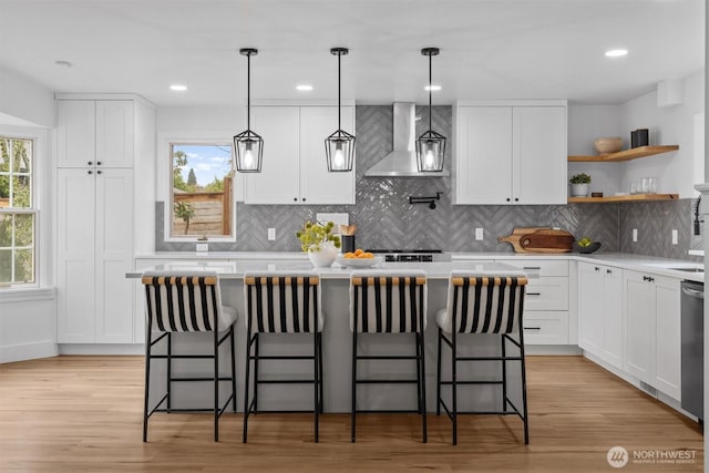 kitchen featuring light countertops, wall chimney range hood, a kitchen island, and white cabinets