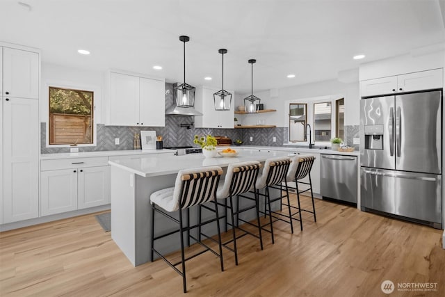 kitchen with appliances with stainless steel finishes, plenty of natural light, wall chimney range hood, and light wood-style flooring