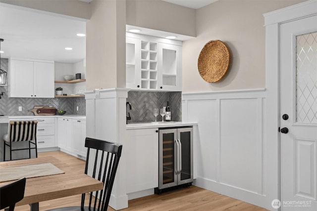 bar with recessed lighting, beverage cooler, wainscoting, decorative backsplash, and light wood finished floors