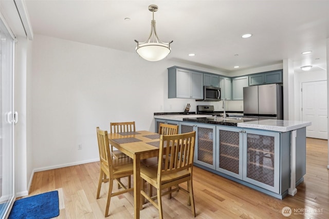 kitchen featuring baseboards, a sink, glass insert cabinets, appliances with stainless steel finishes, and light wood-type flooring