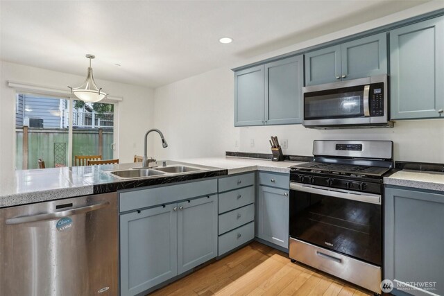 kitchen featuring gray cabinets, a sink, stainless steel appliances, light wood-style floors, and pendant lighting