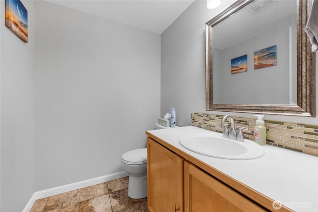 half bathroom featuring toilet, vanity, visible vents, baseboards, and tasteful backsplash