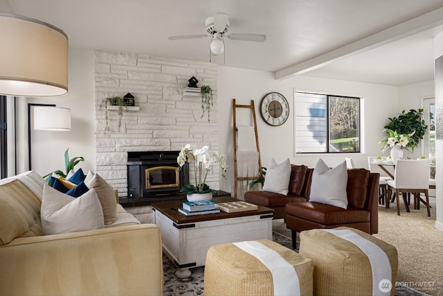 living room with ceiling fan, a stone fireplace, carpet flooring, and beamed ceiling