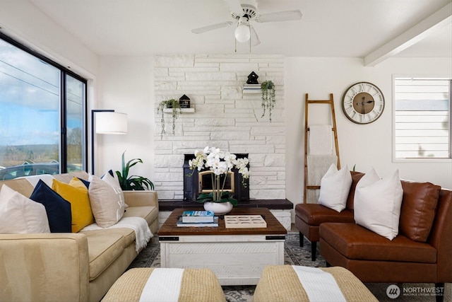 living area with a ceiling fan, beam ceiling, plenty of natural light, and a stone fireplace