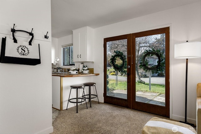 kitchen featuring baseboards, light colored carpet, a kitchen breakfast bar, french doors, and white cabinetry