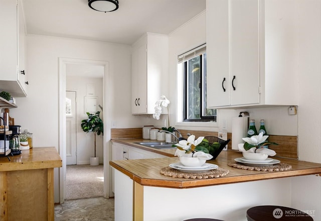 kitchen with ornamental molding, a sink, and white cabinets