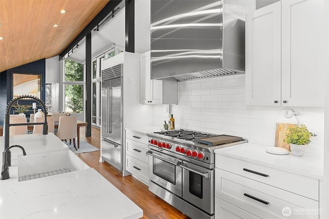 kitchen with decorative backsplash, lofted ceiling, high quality appliances, wood finished floors, and wall chimney range hood