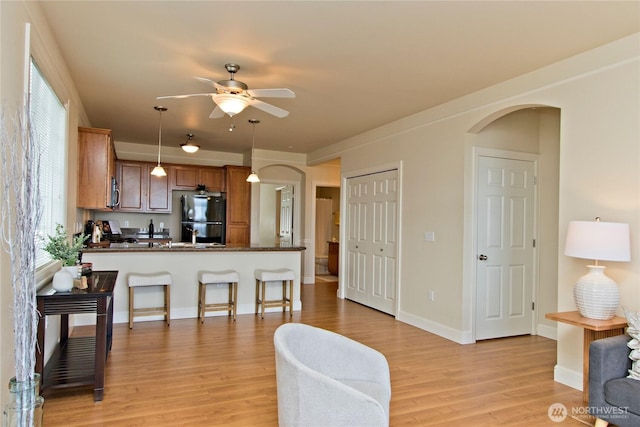 living room with light wood-style floors, arched walkways, baseboards, and a ceiling fan