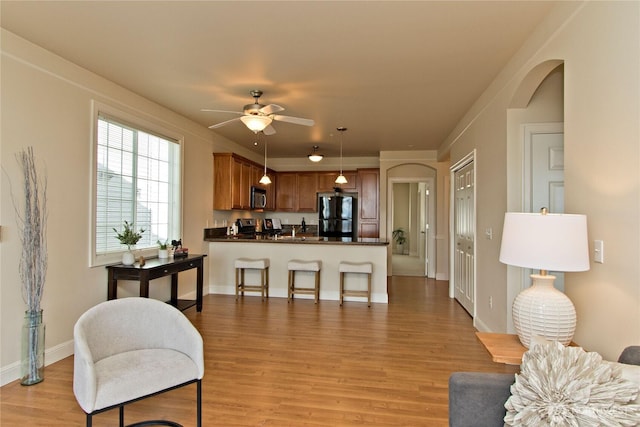 living area with light wood finished floors, baseboards, arched walkways, and a ceiling fan