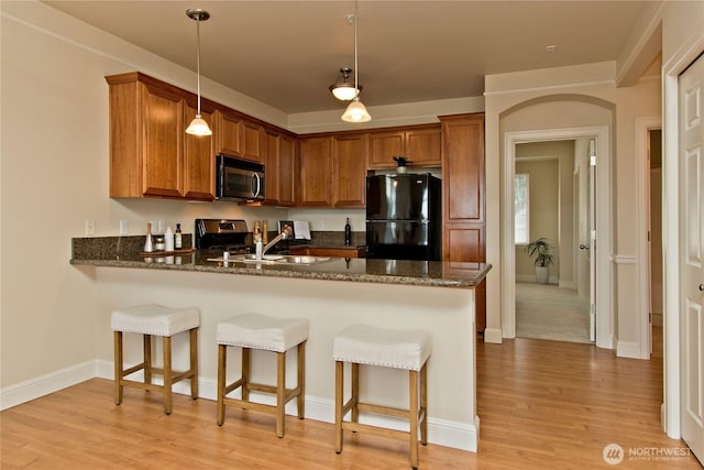 kitchen featuring stainless steel appliances, brown cabinetry, light wood-style flooring, and a peninsula