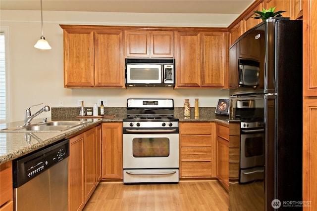 kitchen with brown cabinets, hanging light fixtures, appliances with stainless steel finishes, a sink, and light wood-type flooring