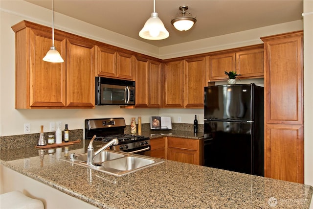 kitchen with dark stone counters, brown cabinets, decorative light fixtures, stainless steel appliances, and a sink