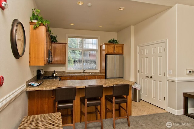 kitchen with freestanding refrigerator, a sink, gas range, black microwave, and a peninsula