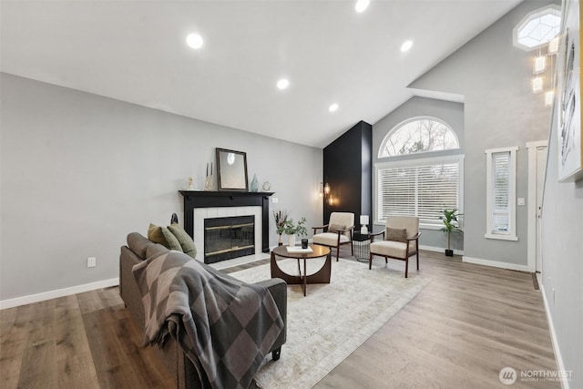 living room featuring baseboards, a fireplace with flush hearth, wood finished floors, high vaulted ceiling, and recessed lighting