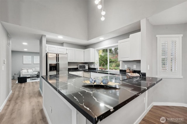 kitchen with appliances with stainless steel finishes, light wood-type flooring, a sink, and a peninsula