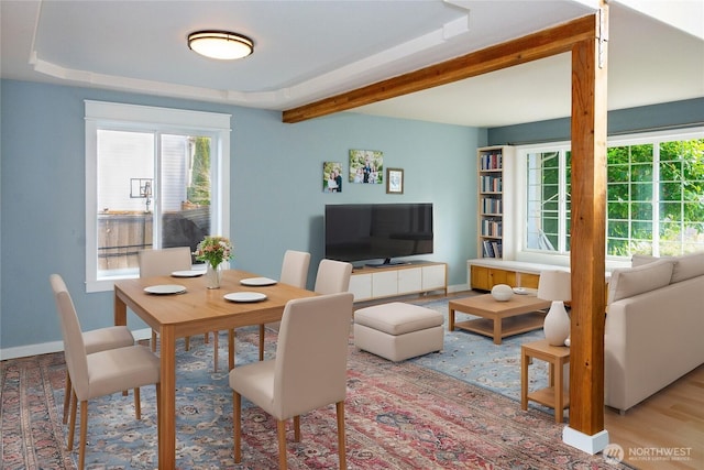 dining space with a tray ceiling, wood finished floors, baseboards, and beam ceiling