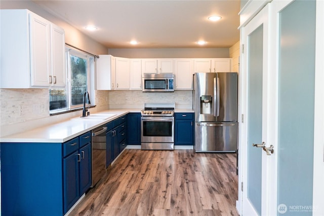 kitchen with light wood finished floors, blue cabinetry, white cabinets, stainless steel appliances, and a sink