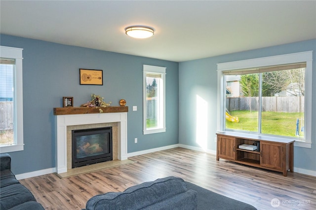 living room featuring a tiled fireplace, baseboards, and wood finished floors