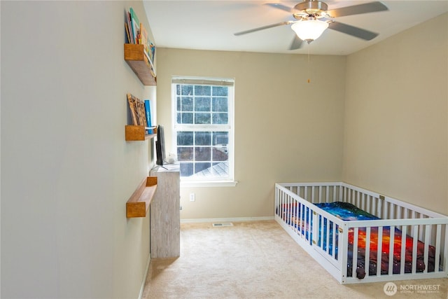 bedroom featuring visible vents, a crib, baseboards, carpet flooring, and a ceiling fan