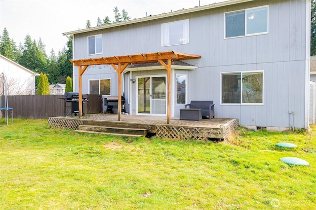 rear view of property featuring a yard, a trampoline, a deck, and fence