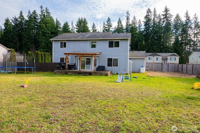 rear view of house featuring a wooden deck, a trampoline, a fenced backyard, and a yard