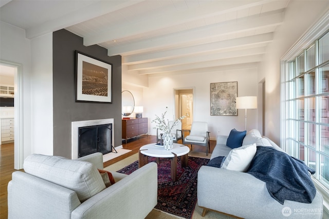 living area featuring beam ceiling, a fireplace with flush hearth, and wood finished floors