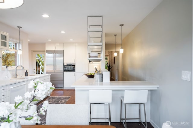 kitchen with light countertops, appliances with stainless steel finishes, a peninsula, white cabinetry, and a sink