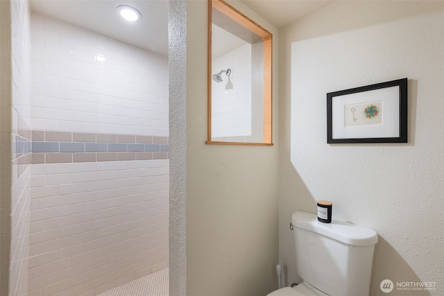 bathroom with toilet, a textured wall, and tiled shower