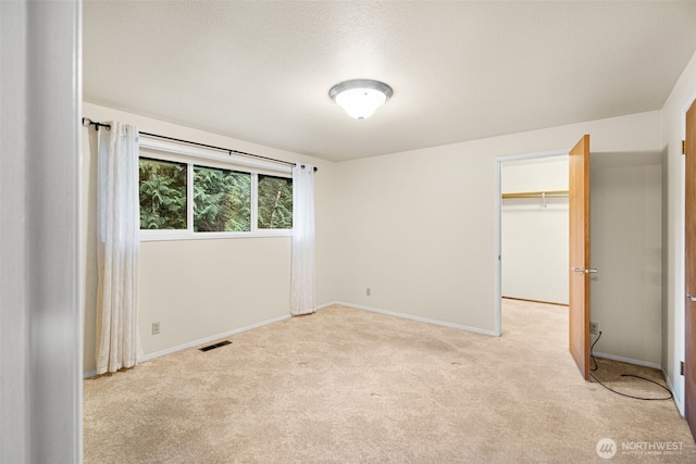 unfurnished bedroom featuring visible vents, a spacious closet, light carpet, a textured ceiling, and baseboards