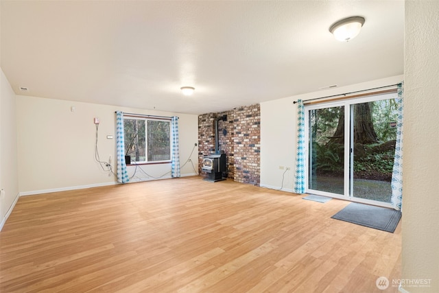 unfurnished living room featuring a wood stove, light wood-type flooring, visible vents, and baseboards