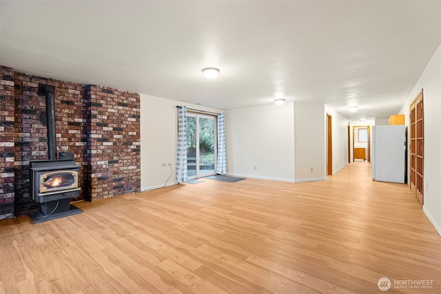 unfurnished living room with a wood stove, light wood-style floors, brick wall, and baseboards