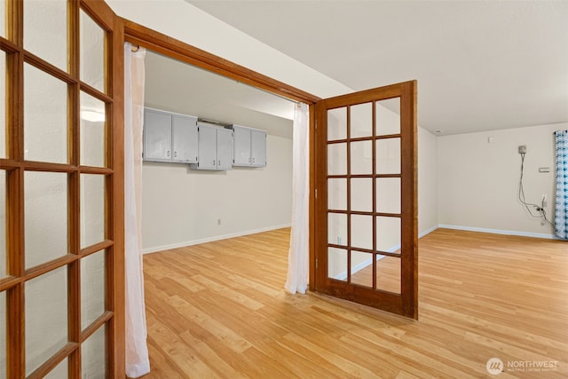 hall featuring light wood-type flooring, vaulted ceiling, and baseboards