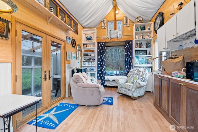 living area featuring lofted ceiling, light wood-style floors, wooden walls, and french doors